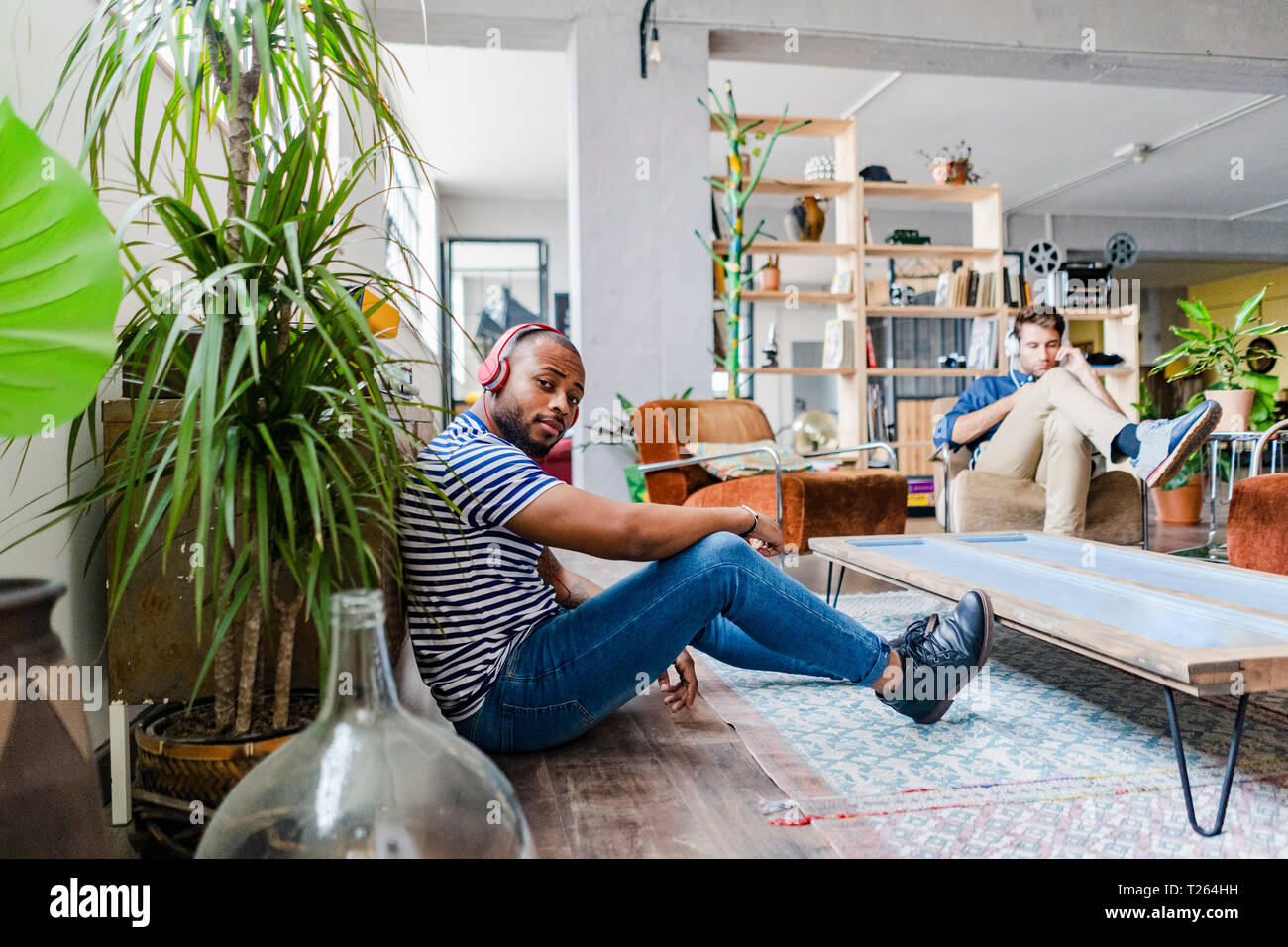 Junger Mann mit Kopfhörer sitzen auf dem Boden in einem Loft Stockfoto