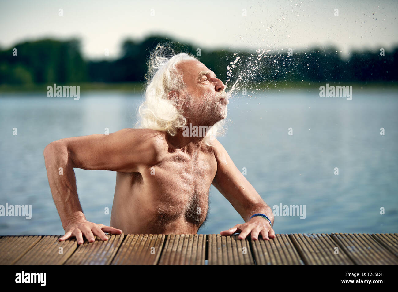 Älterer Mann mit weißem Haar lehnte sich auf Jetty spritzen mit Wasser Stockfoto
