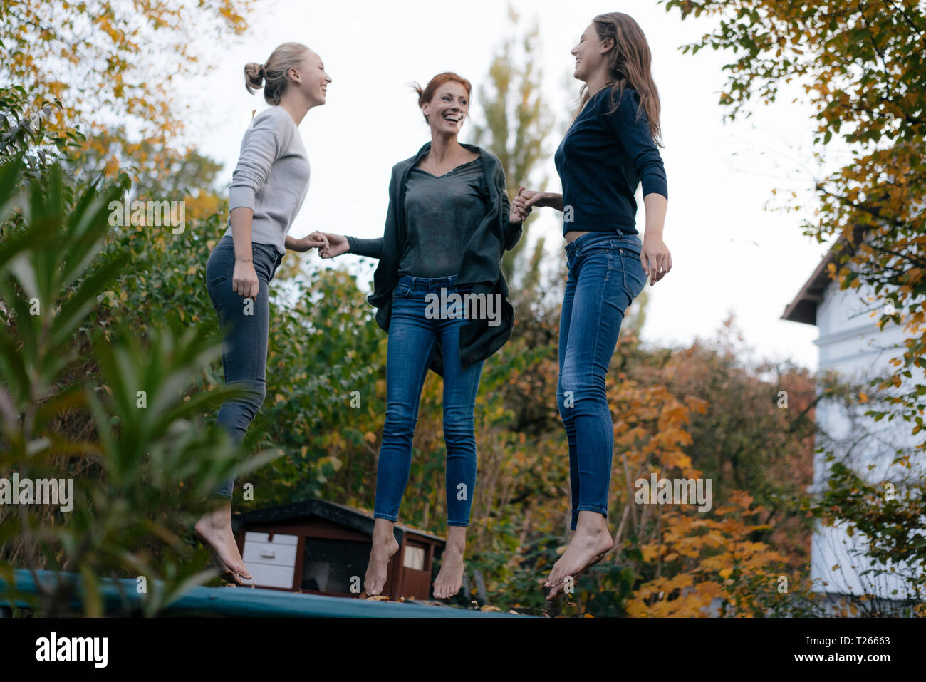 Glückliche Mutter mit zwei Töchtern im Teenageralter springen auf Trampolin im Garten im Herbst Stockfoto