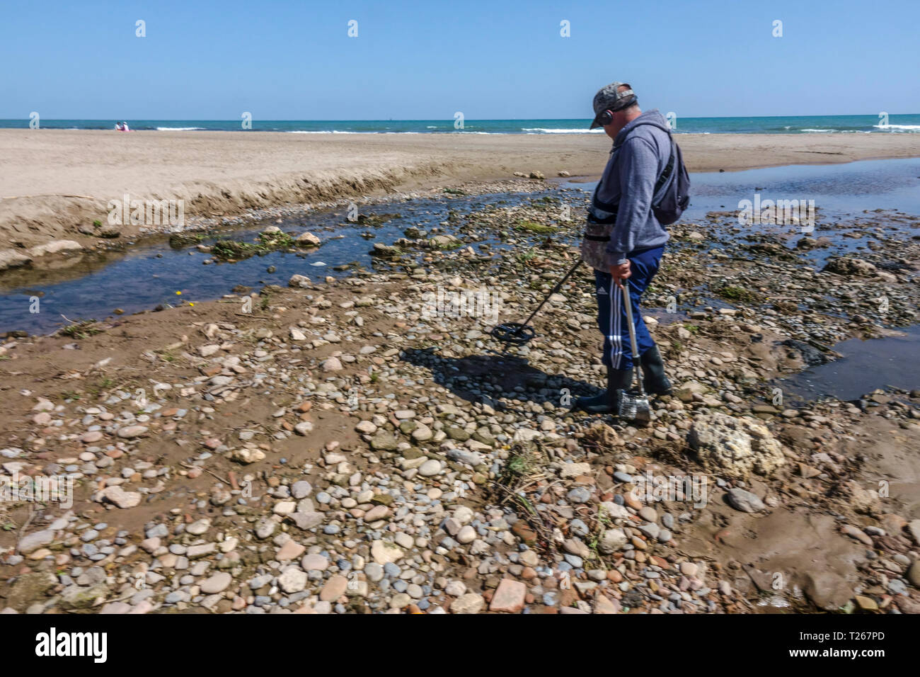 Mann mit einem Metalldetektor kleine Objekte in einem kleinen Flussbett durch das Meer, Valencia, Spanien Stockfoto