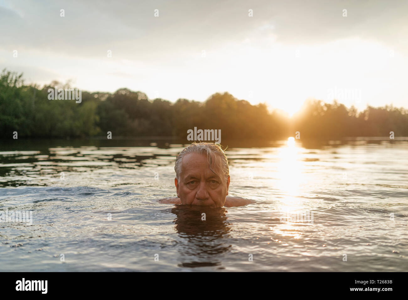 Älterer Mann Schwimmen in einem See bei Sonnenuntergang Stockfoto