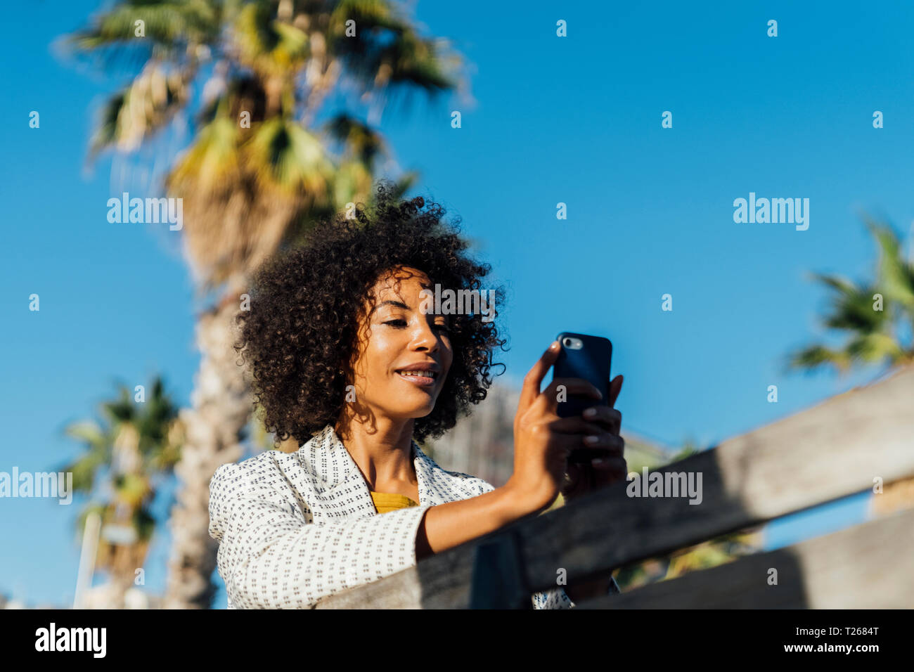 Schöne Frau sitzen auf einer Bank in der Stadt, takig Bilder mit Ihrem Smartphone Stockfoto