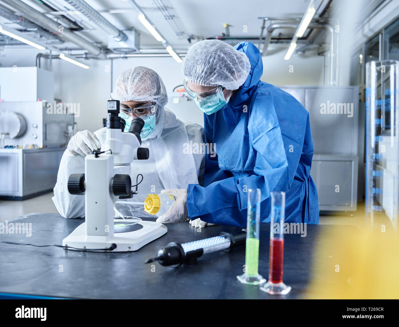 Chemiker in Industrie Labor arbeiten, durch das Tragen von schützender Kleidung und Verwendung von Mikroskop Stockfoto