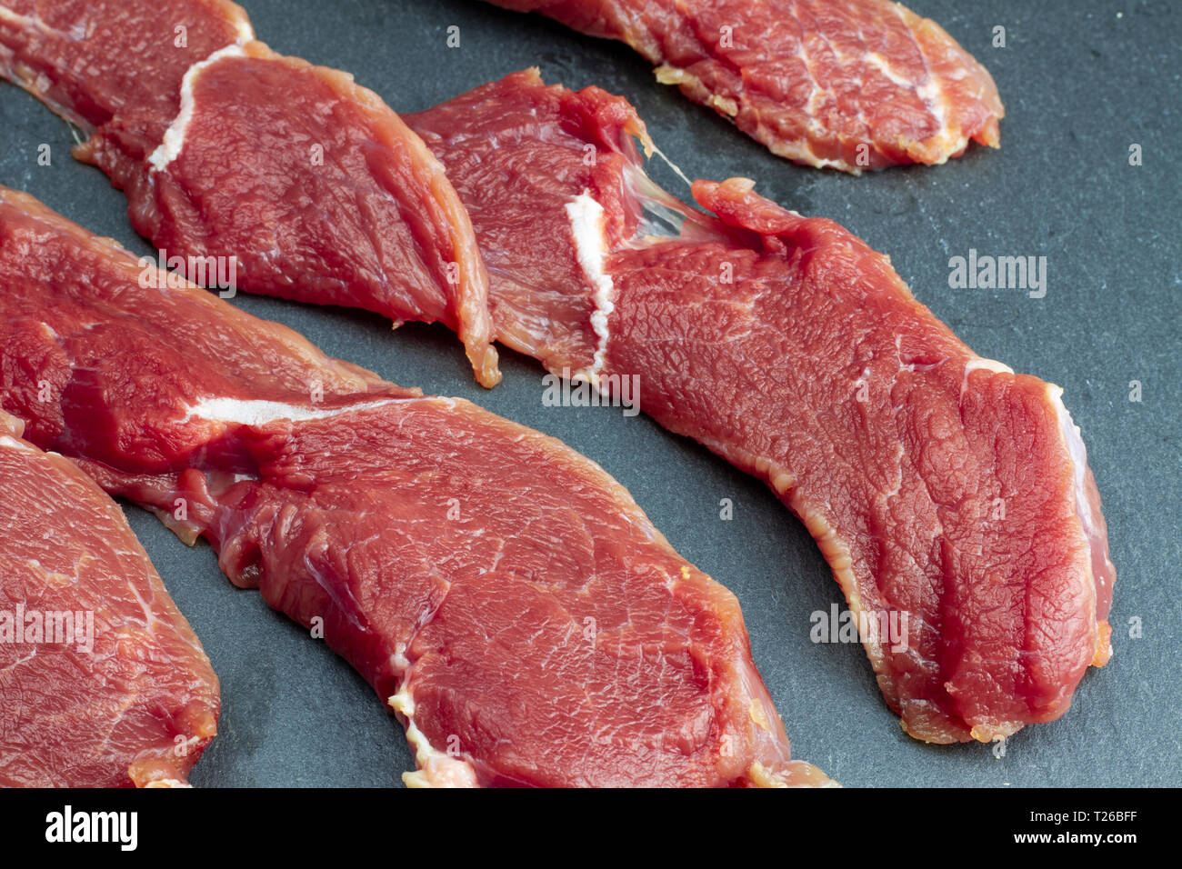 Appetitlich rot frisches Kalbfleisch, in dünne Scheiben geschnitten,  Rindersteaks auf einen schwarzen Stein Schiefer gelegt. Das Rezept für  Kochen Fleisch Steaks. High Definition phot Stockfotografie - Alamy