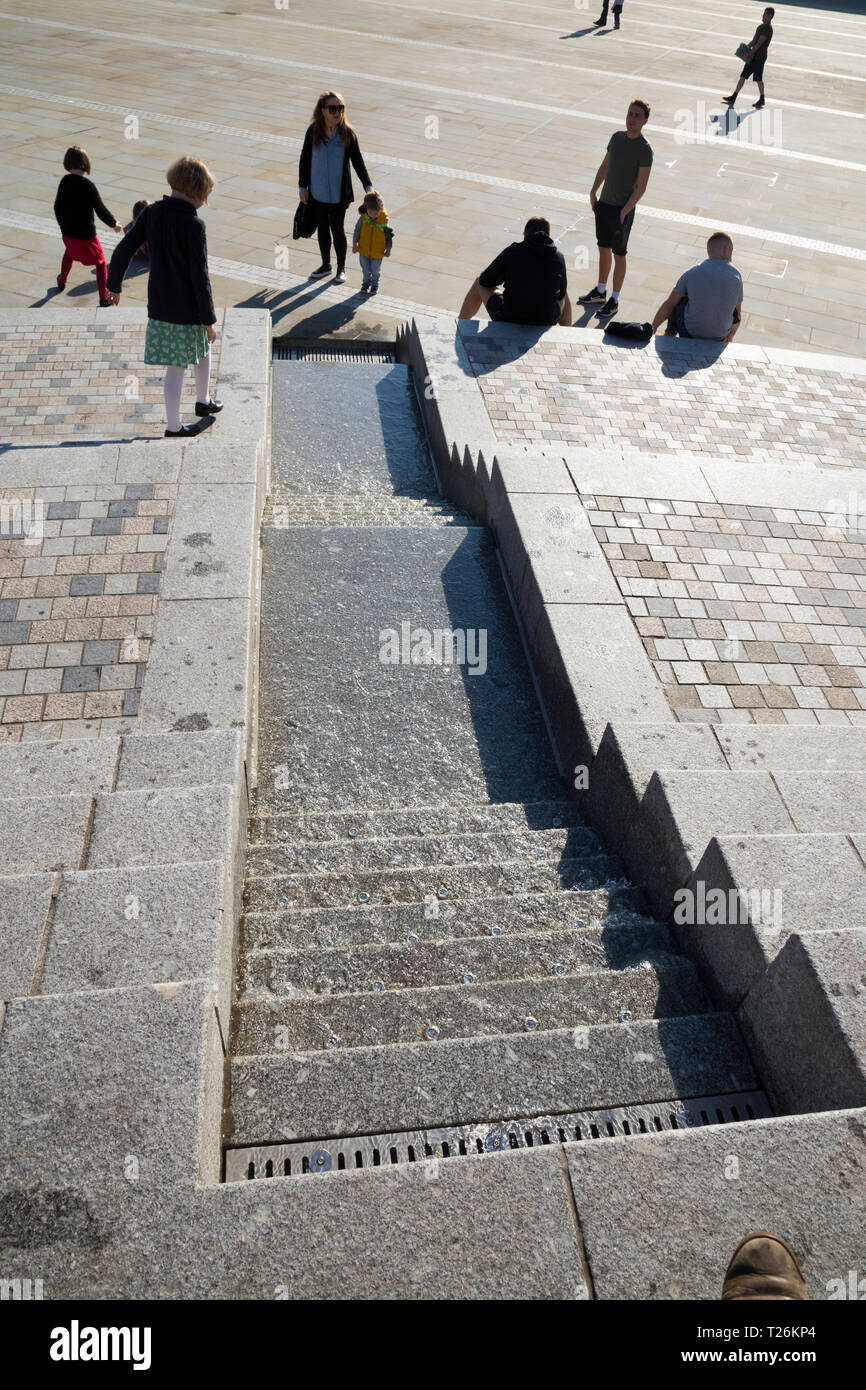 Kind spielt rund um die Wasser- und Besucher/Touristen sitzen und auf den Stufen im Viereck des wiederhergestellten Piece Hall entspannen. Sonnigen Tag/sun. Halifax, England Großbritannien Stockfoto