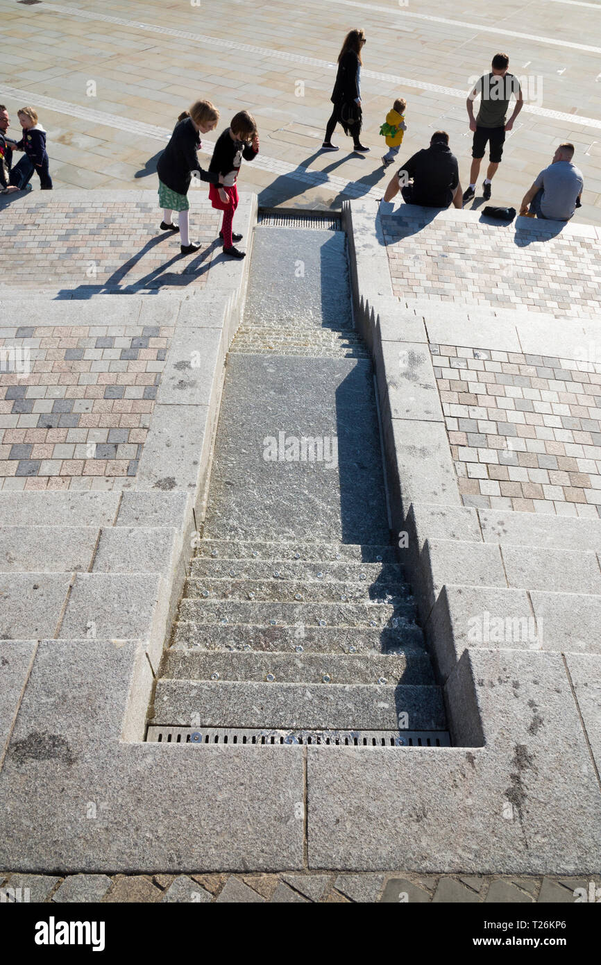 Kind spielt rund um die Wasser- und Besucher/Touristen sitzen und auf den Stufen im Viereck des wiederhergestellten Piece Hall entspannen. Sonnigen Tag/sun. Halifax, England Großbritannien Stockfoto