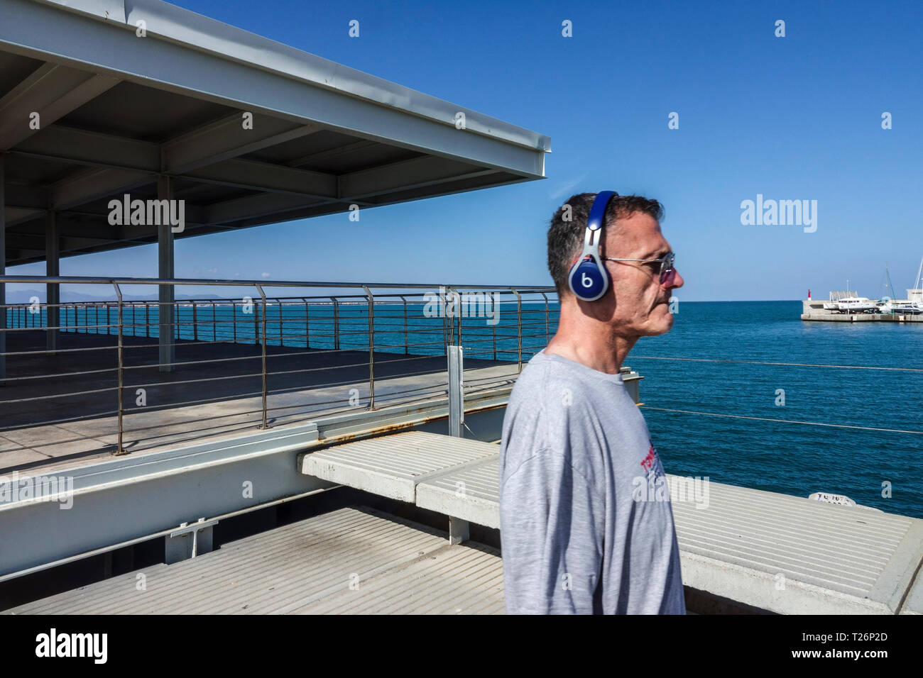 Kopfhörer Senioren Mann auf dem Betonpier Meer hinten Valencia Port Spanien Senioren Erwachsene 50er Jahre hören Musik Senioren Musik Ohrhörer für Erwachsene Stockfoto