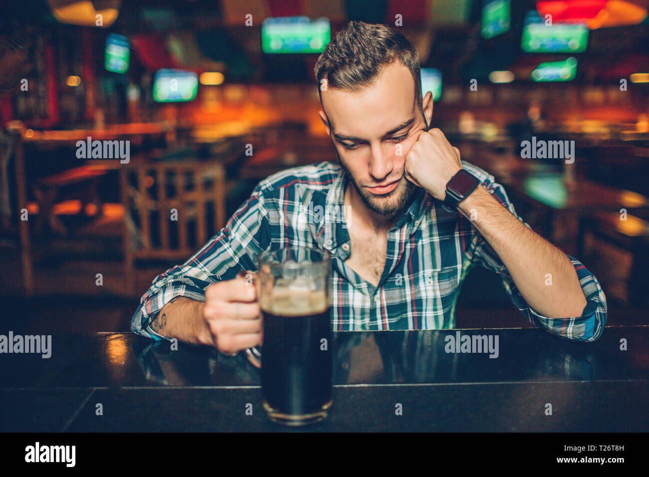 Allein junge Mann an der Theke in der Kneipe sitzen. Er schlafen. Junger Mann halten die Hand auf Tasse mit dunklem Bier Stockfoto