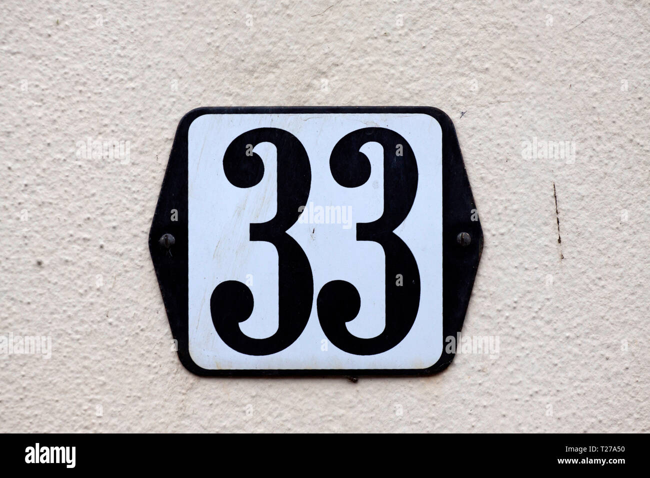 Weiß mit schwarz lackierter Haus platte Nummer 33 wird auf eine weiße Wand Stockfoto