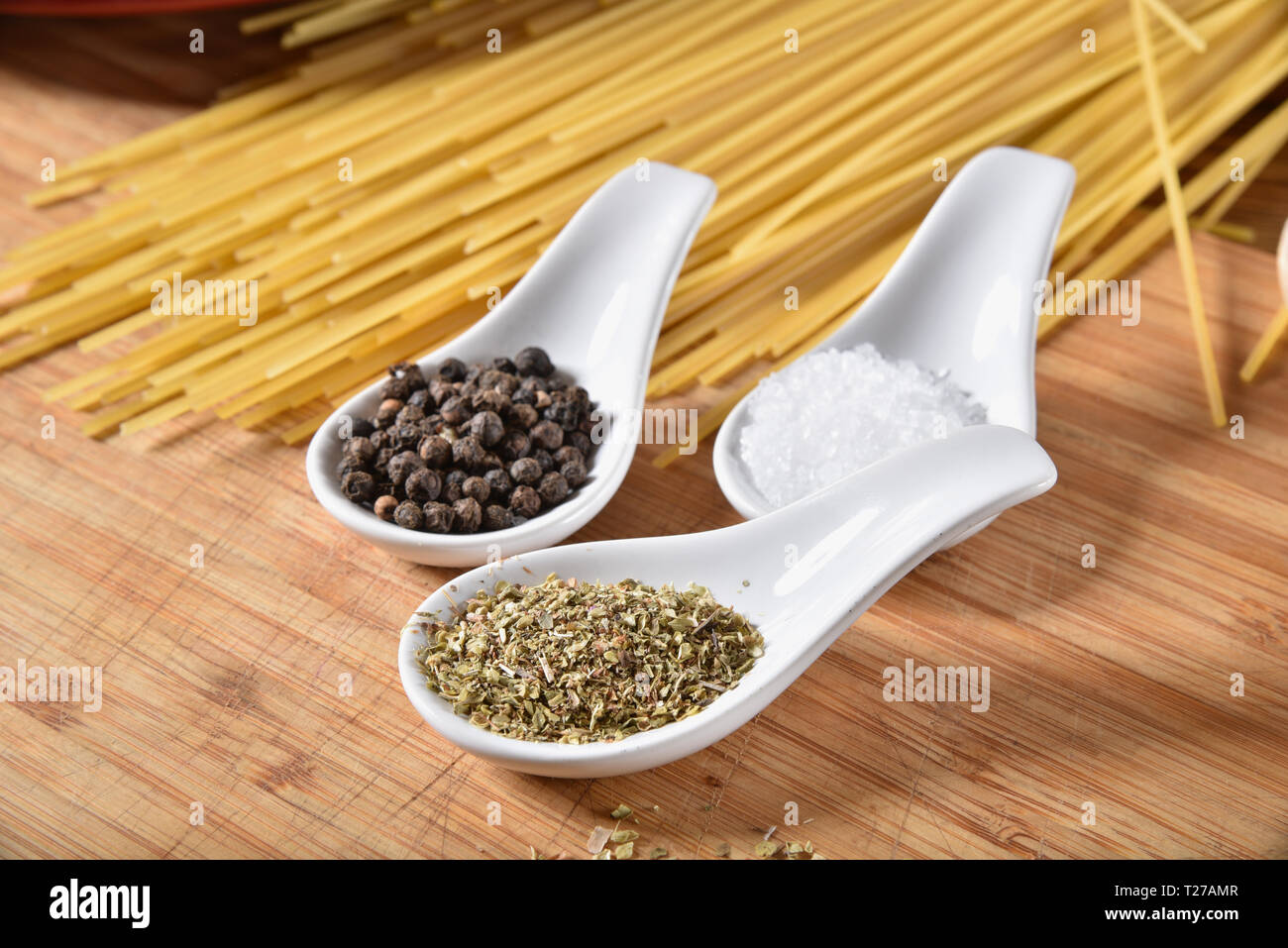 Teelöffel Oregano, Pfeffer und Salz auf einem Schneidebrett mit spaghetti Nudeln Stockfoto