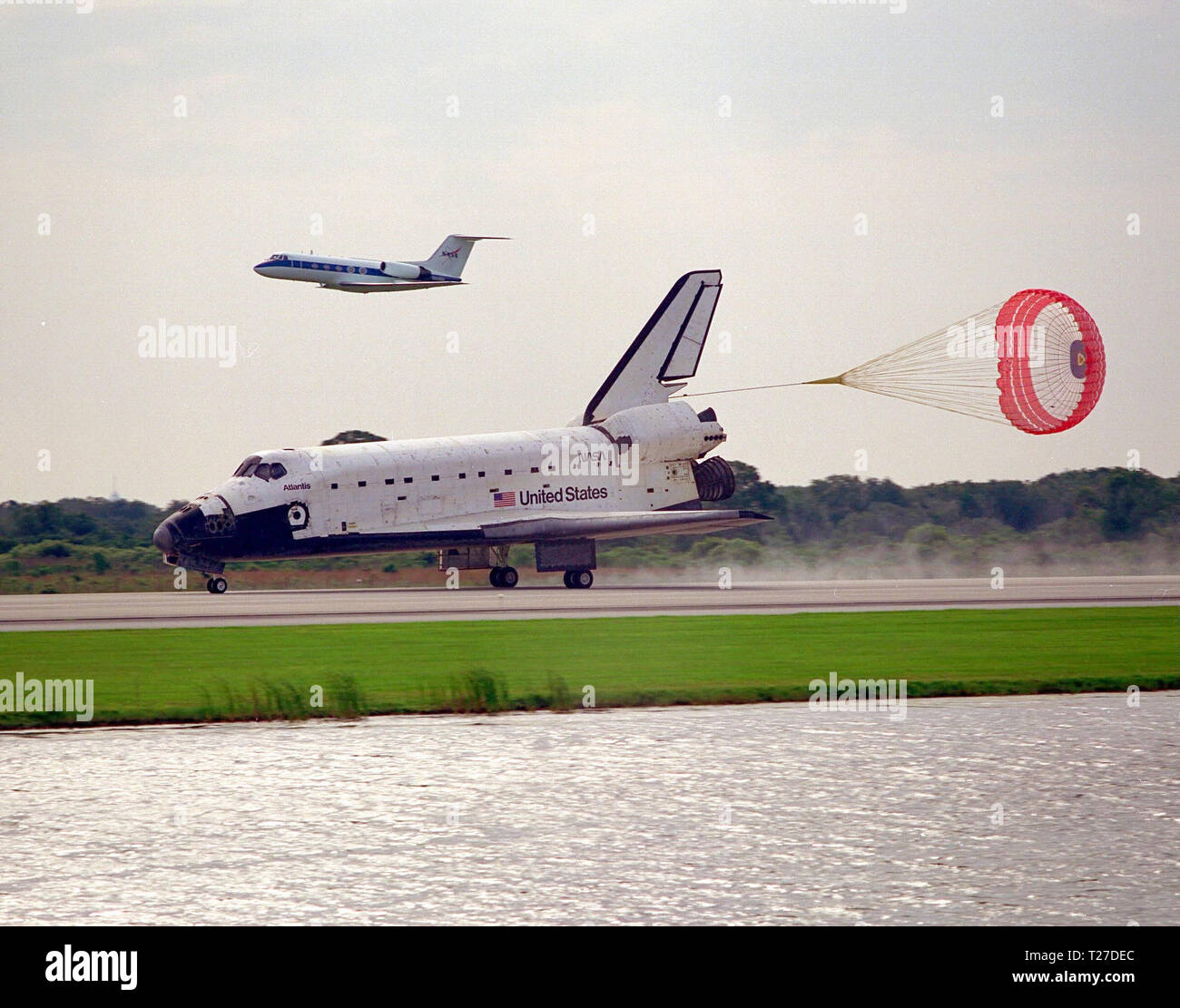 Das Space Shuttle Orbiter Atlantis, mit der Rutsche ziehen eingesetzt, rollt auf der Piste 33 des KSC Shuttle Landing Facility am Ende der neun-tägigen Mission STS-84. Der Shuttle Schulungsflugzeug von Astronauten Kenneth D. Cockrell, stellvertretender Leiter des Astronautenbüros, fliegt über Atlantis. Main gear Touchdown war bei 9:27:44 CEST am 24. Mai 1997. Stockfoto