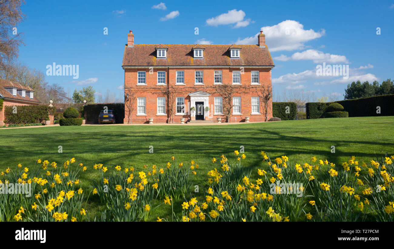 Elegante englische Country Manor Herrenhaus Grad 2 Viktorianischen zeit Immobilien in rotem Backstein aufgeführt. Vorderansicht mit großem Garten, grünen Rasen und daffod Stockfoto
