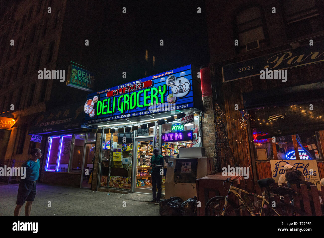 New York City, USA - 29. Juli 2018: Schwarzer Mann verlassen ein Lebensmittelgeschäft in der Nacht neben einer Terrasse der Bar mit einem Drink auf Sommer in Harlem, Stockfoto