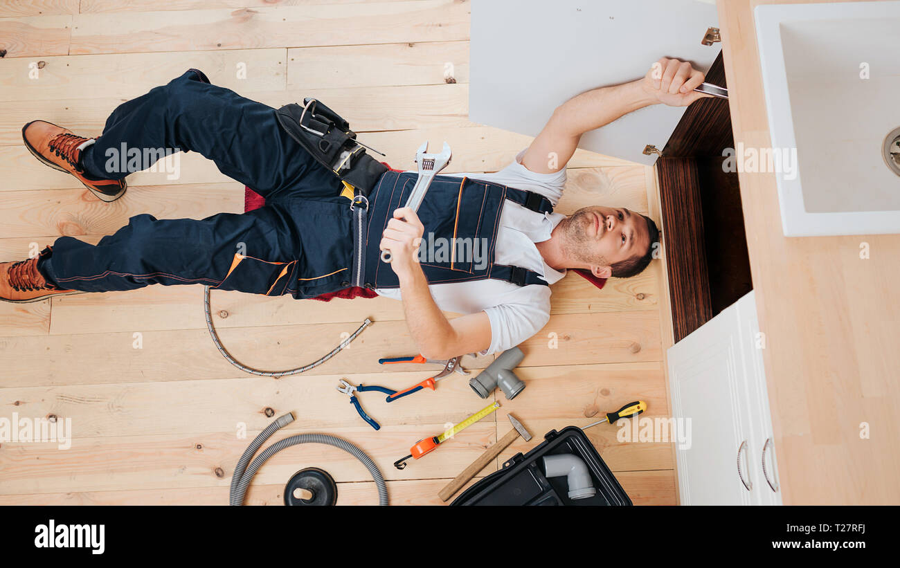 Konzentriert beschäftigt Klempner Befestigung auf in der Küche unter der Spüle. Er lag auf dem Boden. Kerl halten Schraubenschlüssel Stockfoto