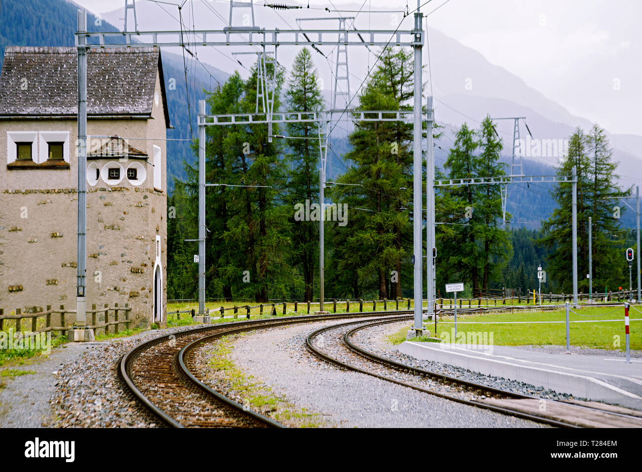 Alte Schmalspurbahn in das Tal der Alpen unter den Bäumen bei bewölktem Himmel. Stockfoto