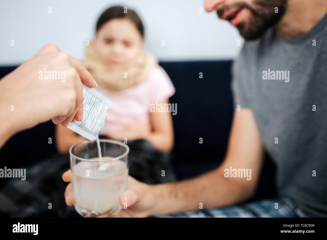 Schnittansicht des Doctor's Hand gießen Pulver Medizin ins Glas Wasser. Junger Mann hld. Kleines krankes Mädchen sitzen auf dem Sofa und Blick auf Prozess Stockfoto