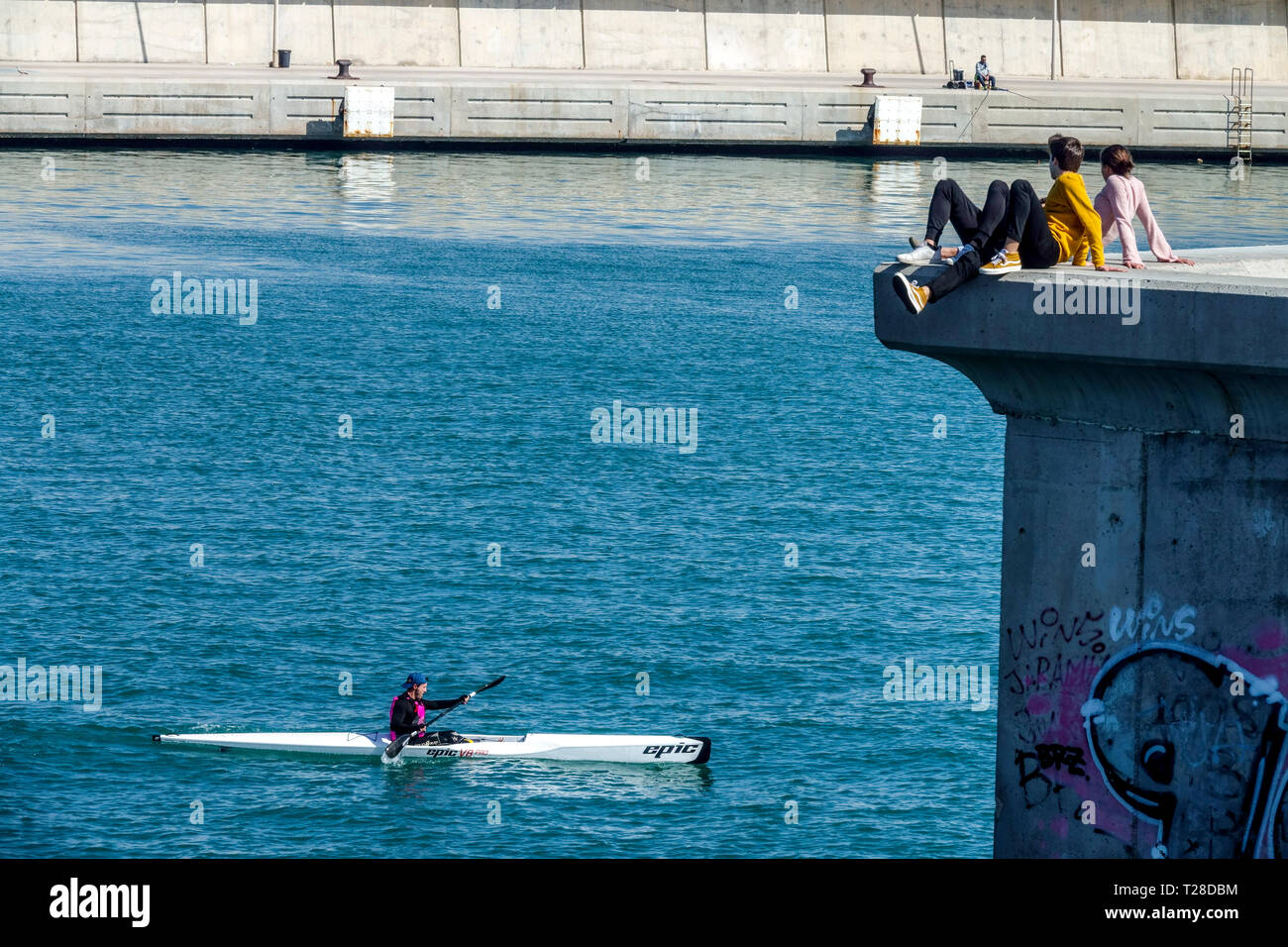 Ein Kajak-Mann betritt einen ruhigen Hafen. Vom Pier beobachten ihn junge Menschen, Valencia Port Spanien Stadt Lebensstil Stockfoto