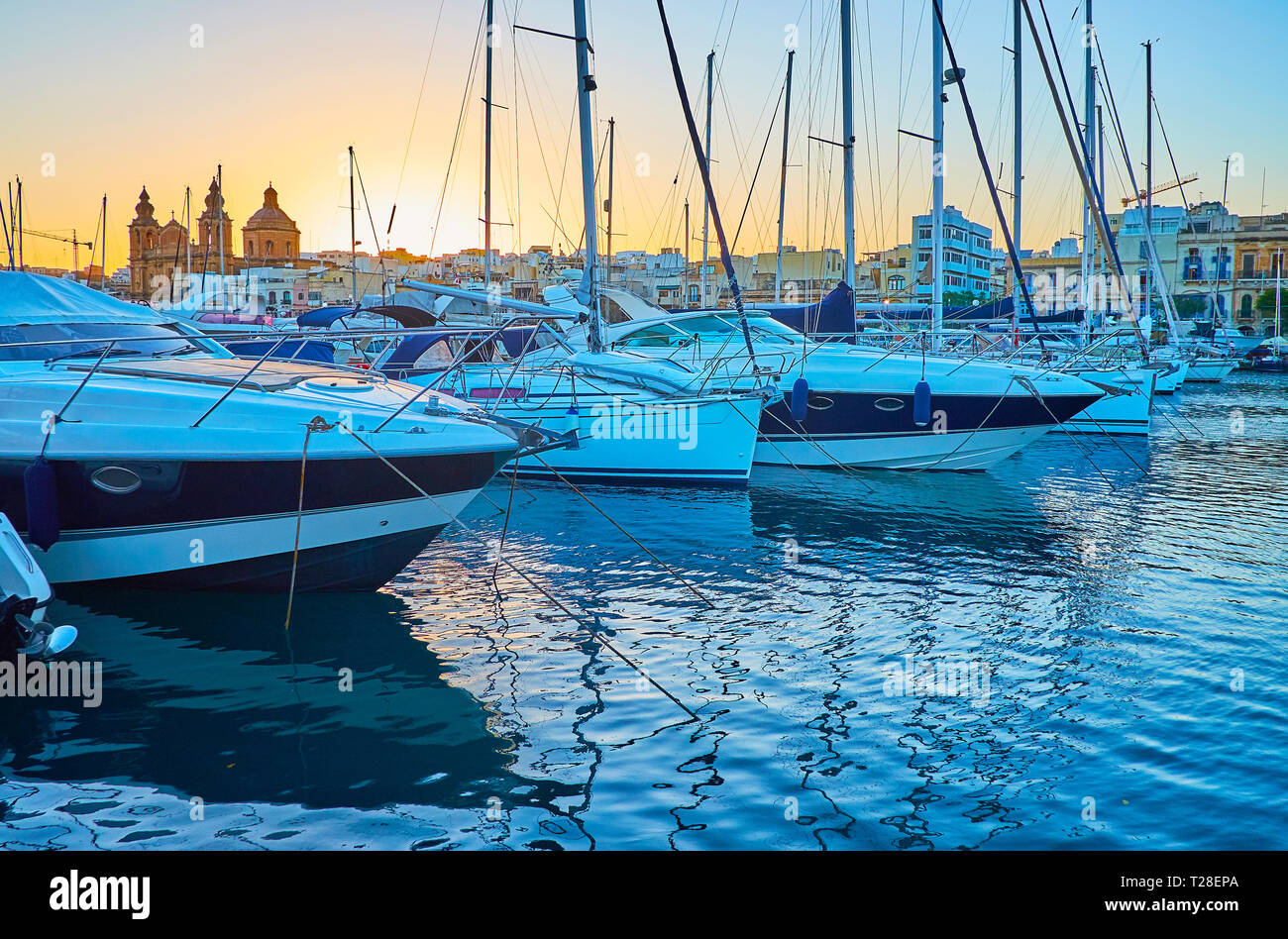 Die Strandpromenade von Pieta Gesichter Msida Marina mit zahlreichen Segelyachten, Motorboote und die Skyline der Stadt in den letzten Strahlen der untergehenden Sonne, Malta. Stockfoto