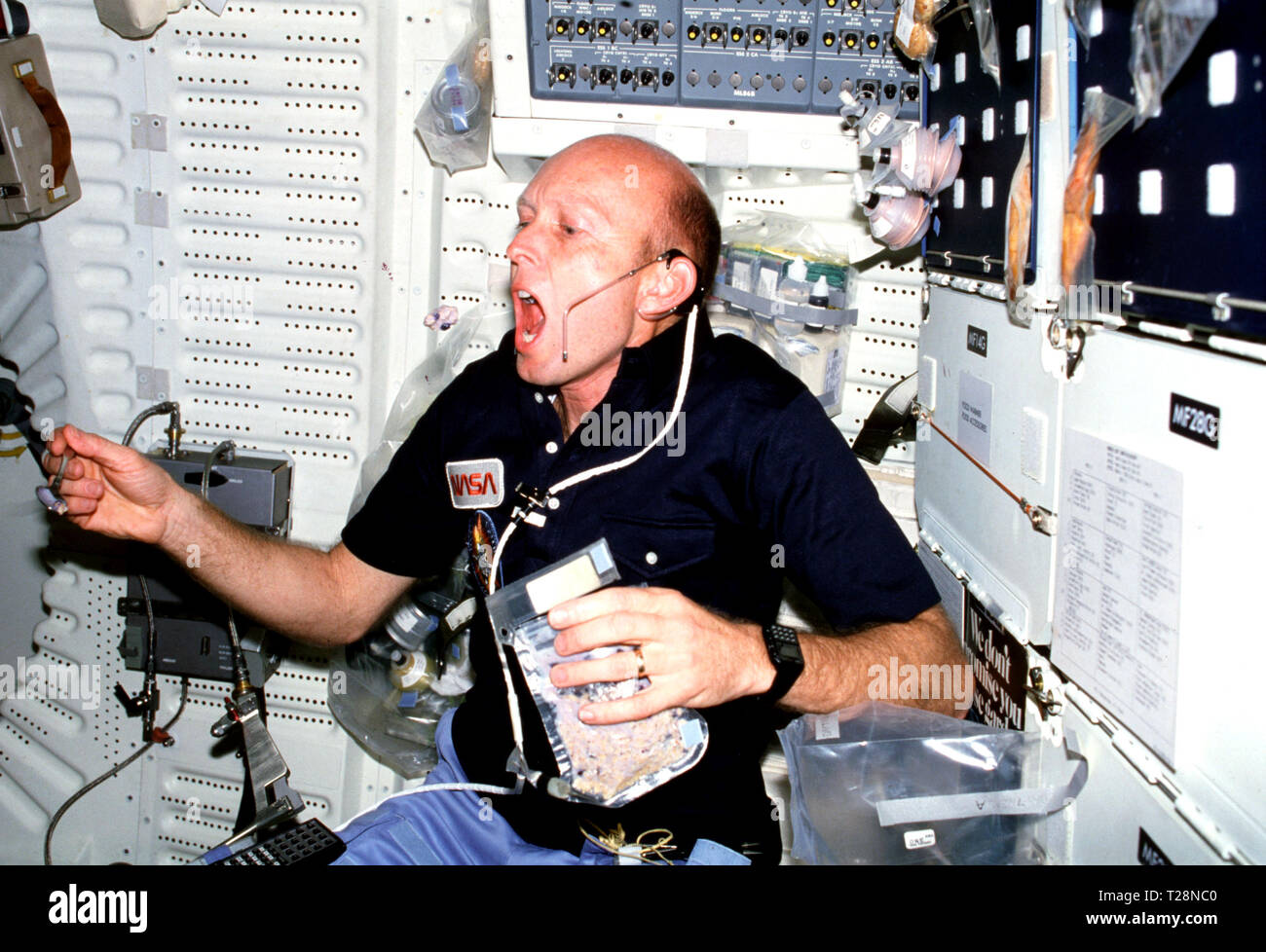 (26 März 1982) --- aus der Luft, Astronaut C. Gordon Fullerton, Pilot, greift sich einen Bissen von Getreide, das er gerade aus einem Kunststoff food Container auf dem Space Shuttle Columbia Mitte spooned hatte-Deck. Fullerton, Pilot für drei Anflug und Landung Tests (ALT) mit dem Space Shuttle Enterprise, bildete seine erste echte Raumfahrt und hatte nie zuvor erlebt Schwerelosigkeit. Astronaut Jack R. Lousma, mission Commander, ausgesetzt, die in diesem Rahmen mit einer 35-mm-Kamera. Stockfoto