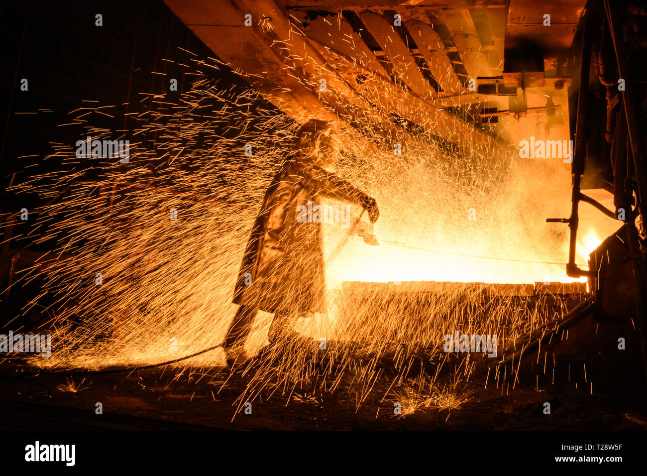 Ein Arbeiter in einem Feuer Anzug gesehen, die Überwachung der Fluss der heißen Flüssigkeit Metal wie er fließt von einem Ofen in der Anlage. Die Produktion von Matt Nickel am PT Vale nickel Pflanze, in Sorowako, Südsulawesi, Indonesien, das Werk zielt eine Produktion von 75.000 Tonnen im Jahr 2019. Stockfoto