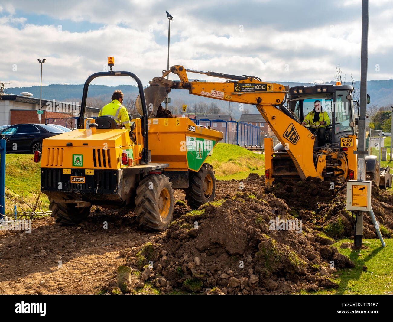 Arbeiter mit einem JCB 3CX Hydraulikbagger laden ausgehobenen Mutterboden in einen Kipper für den Ausbau Stockfoto