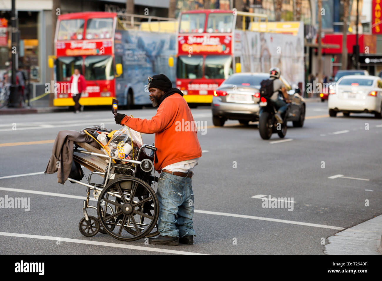 LOS ANGELES - ein obdachloser Mann seine Sachen, die in einem Rollstuhl überquert die Straße auf dem Hollywood Boulevard. Stockfoto
