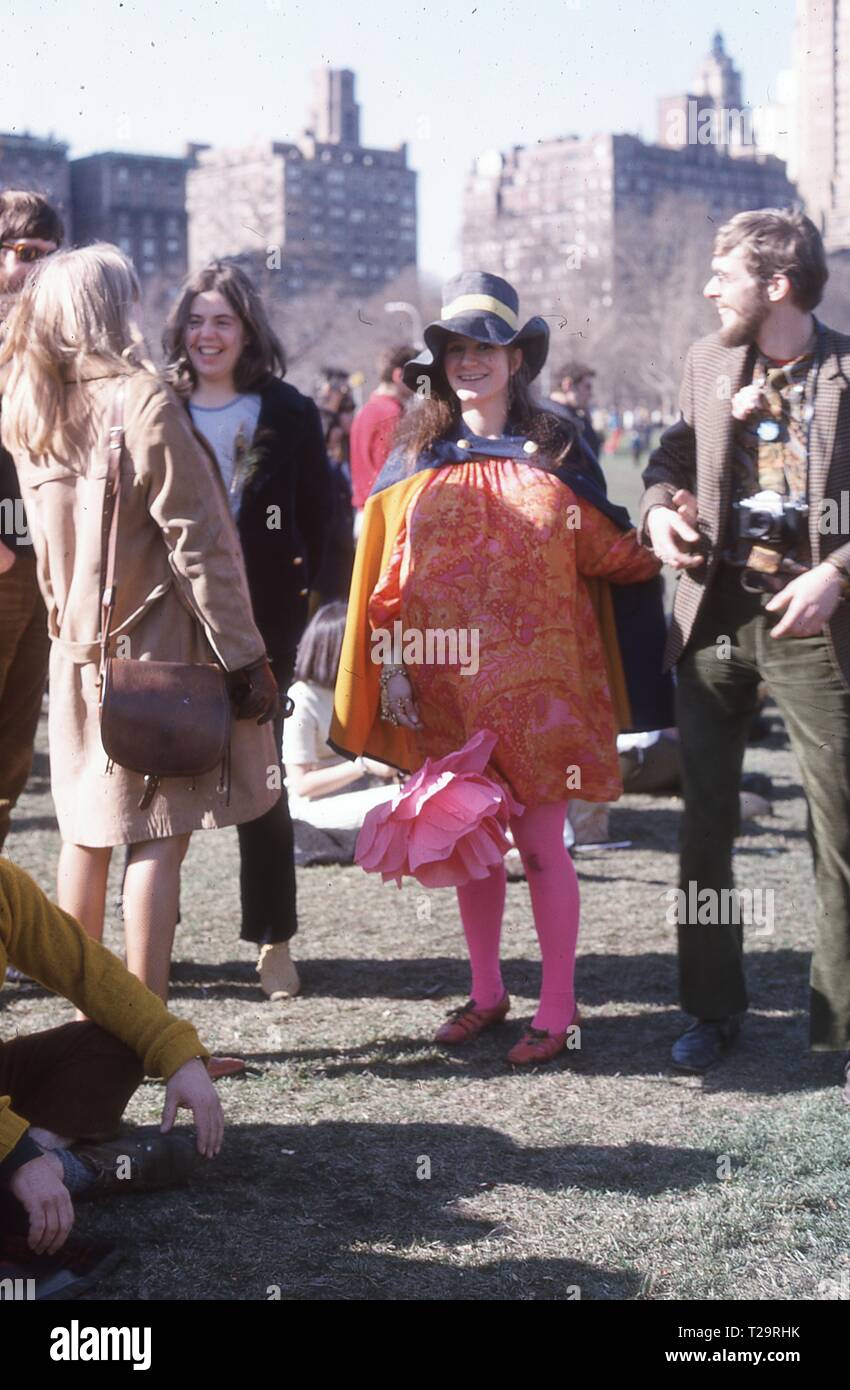 In voller Länge Schuß eines hippie Mädchen in einem extravaganten Kleid, mit einem großen, rosa Blume, die Teilnahme an der Be-In Proteste im Central Park, New York City, März 1967. () Stockfoto