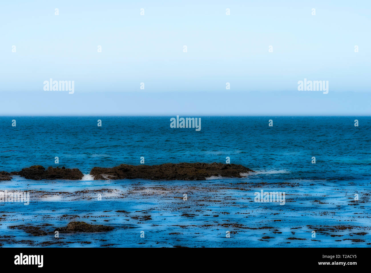 Poster style Bild der blauen Ozean mit Felsen und kleinen Wellen unter Blau grauen Himmel. Stockfoto