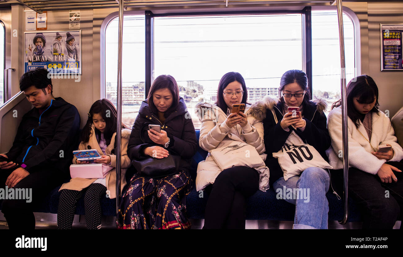 Reihe der Leute sitzen auf dem Zug auf Tokyo Underground, jede Person, die entweder mit Smartphone oder elektronischen Gerät, Tokio, Japan Stockfoto