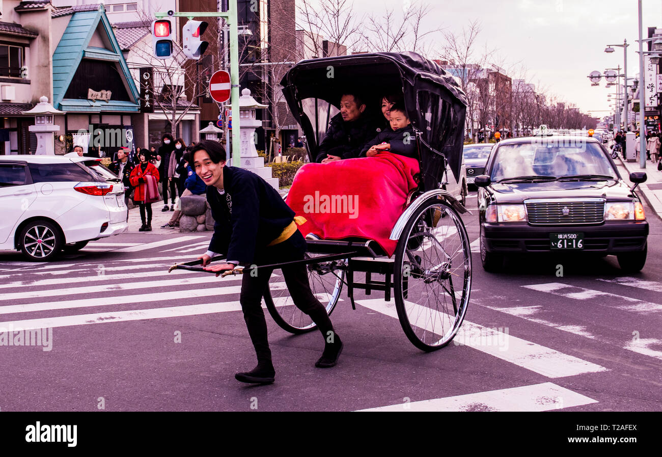 Familie Rikscha-fahrt in belebten Straße, rikscha Fahrer Kamera suchen, lächelnd, Kamakura, Japan Stockfoto