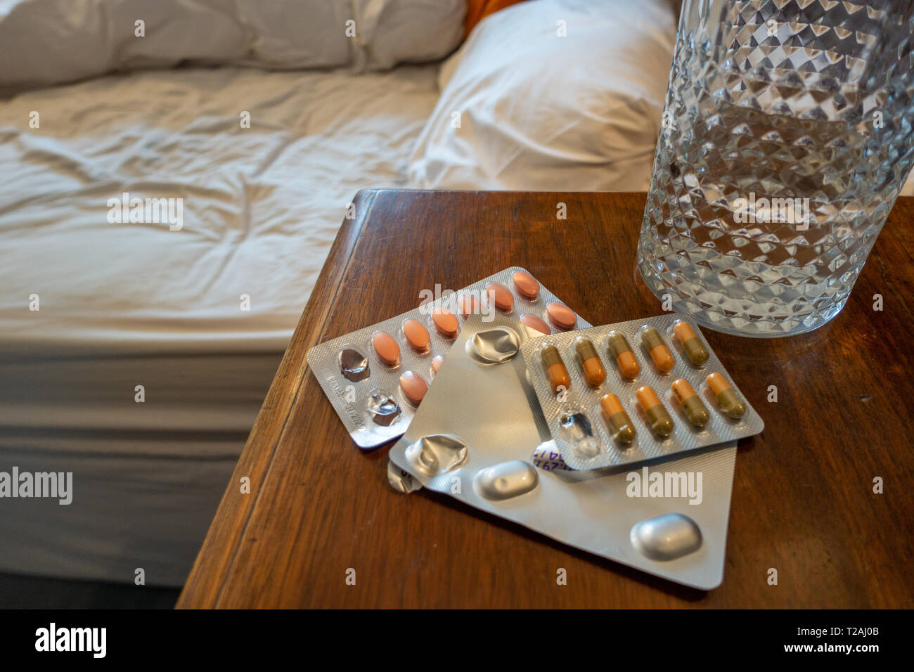 3 Pakete von verschreibungspflichtigen Medikamenten und ein Glas Wasser auf dem Nachttisch Stockfoto