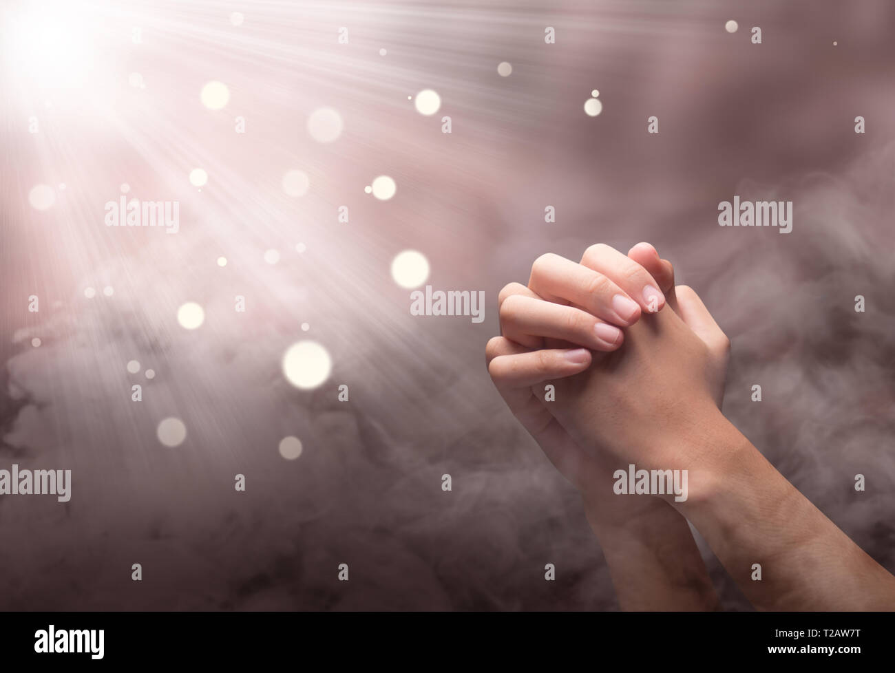 Männliche Hände im Gebet Position mit Ray über verschwommenen Hintergrund Stockfoto