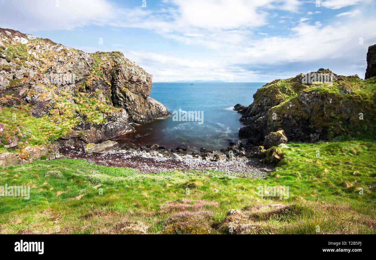 Eine kleine Bucht in einer felsigen Küste bietet Zugang zu einem kleinen, felsigen Strand auf der Insel Islay, Schottland, Großbritannien. Stockfoto