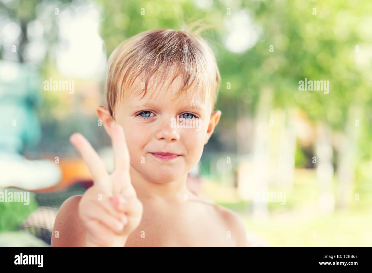 Süße kleine kaukasischen blonde Junge lächelnd und mit Frieden Zeichen mit den Fingern. Kind, das Sieg Geste von Arm. Glückliche Kindheit und Sommerferien. Stockfoto