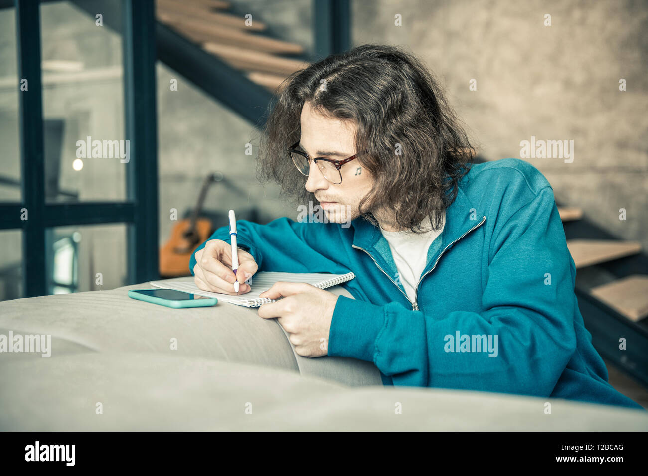 Aufmerksame langhaarigen Kerl mit langen Haaren rewriting Notizen in Album Stockfoto