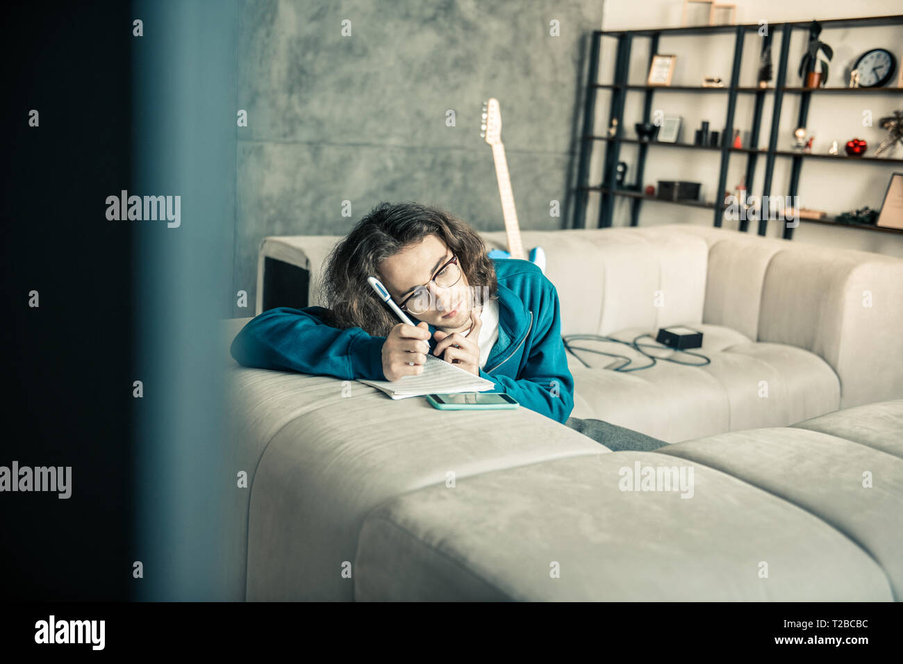 Müde junge Dunkelhaarige Musiker lehnte sich auf der Couch und Schreiben nach unten Stockfoto