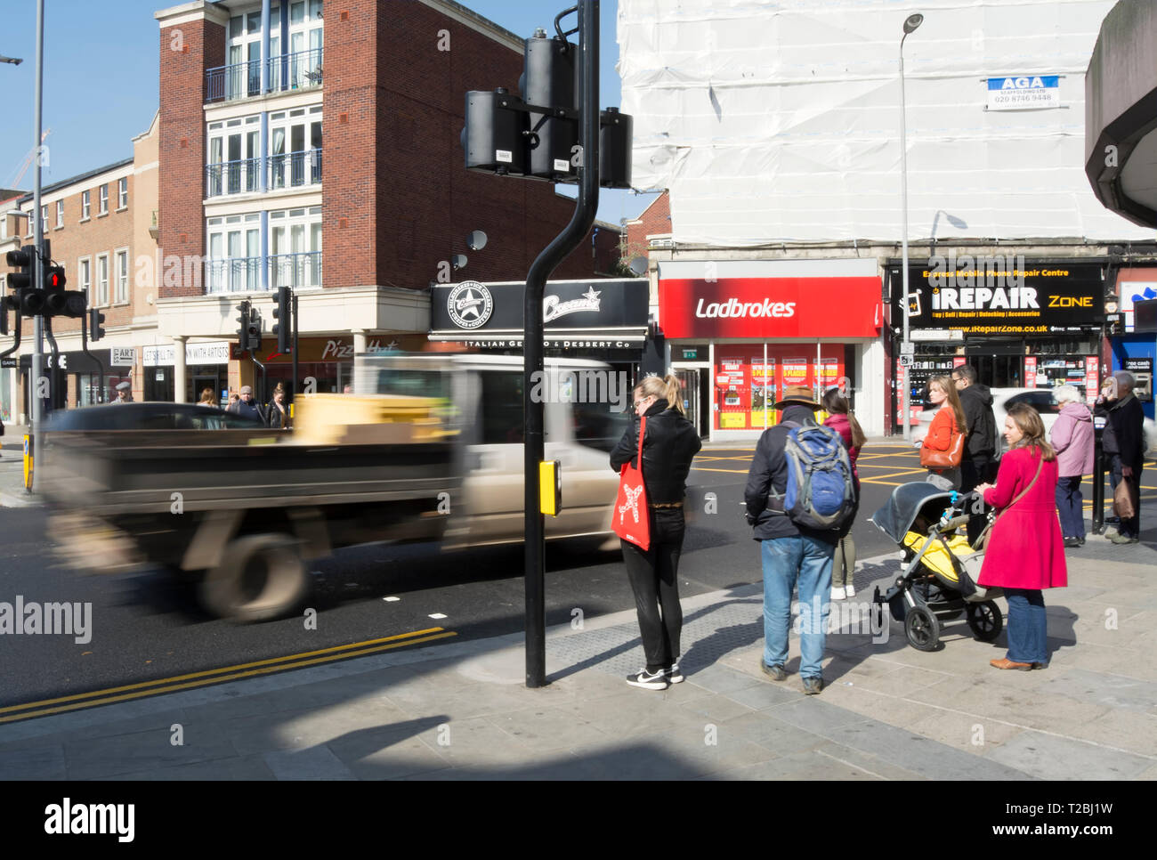 In verschwommene Bewegung gesehen, ein Fahrzeug passiert Fußgänger warten die Straße in Kingston upon Thames, Surrey, England Stockfoto