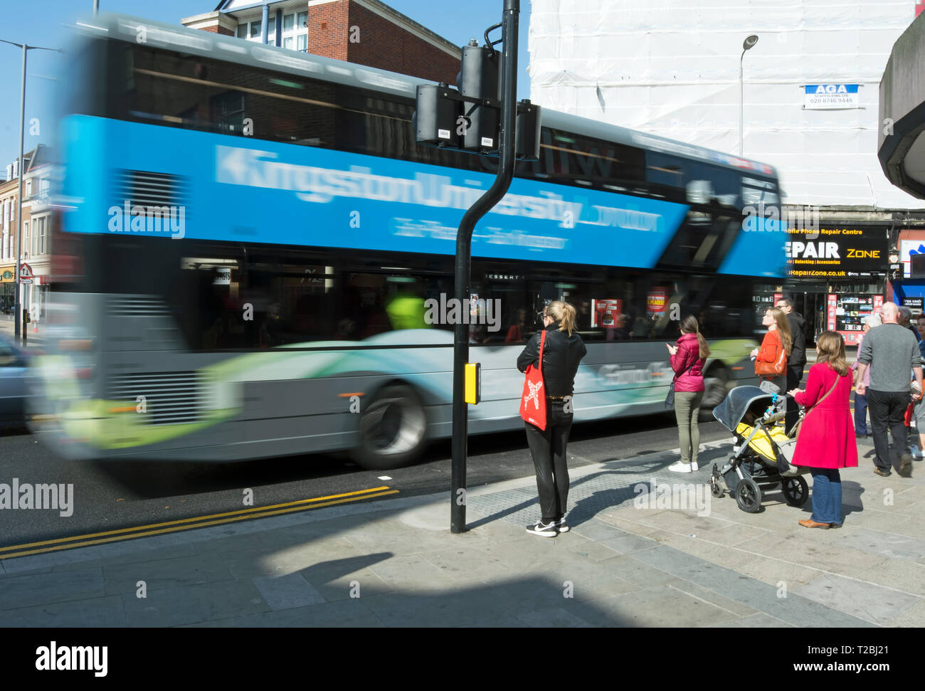 In verschwommene Bewegung gesehen, eine Kingston Universität bus fährt Fußgänger auf der Straße in Kingston upon Thames, Surrey, England Stockfoto
