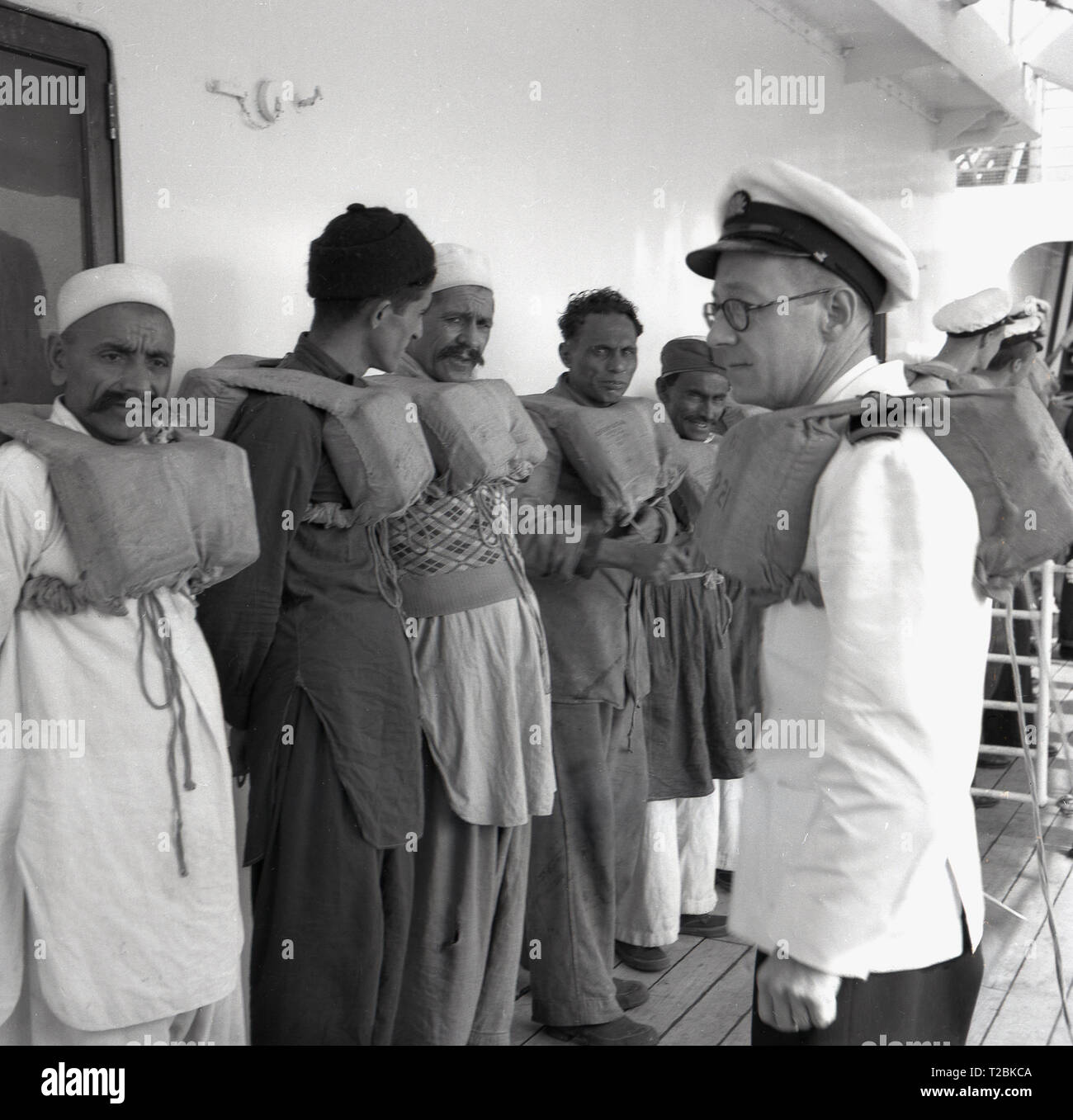 1950, historische, Skipper instructioning ausländische Besatzungsmitglieder auf der P&O SS. Chusan Steamship, wie sie für eine Sicherheit Übung auf Deck mit Schwimmwesten pepare. Stockfoto