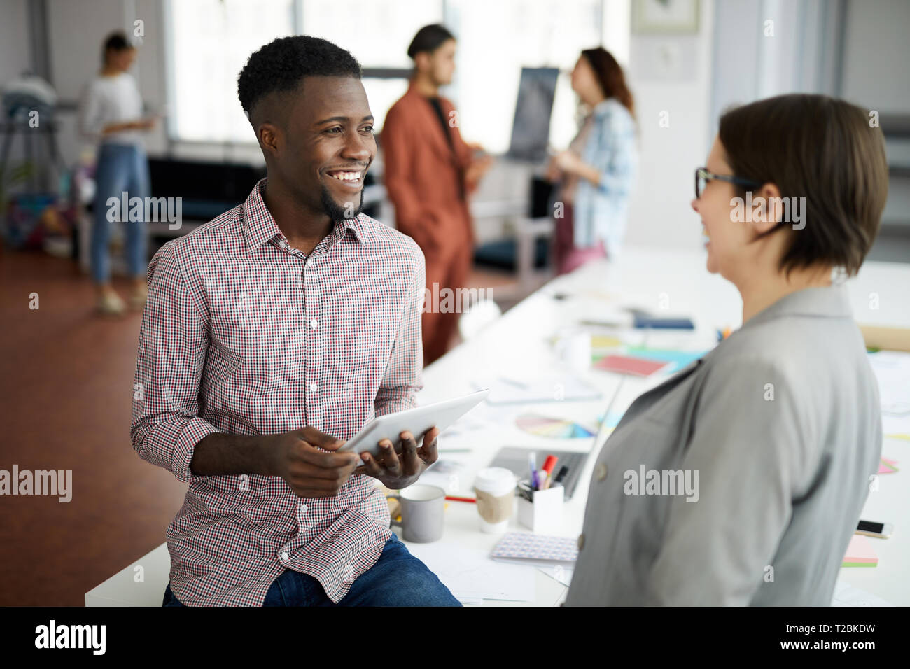 Portrait von stattlichen Afro-amerikanische Mann im Gespräch mit Kollegen und lächelnd, während im modernen Büro, Kopie Raum Stockfoto