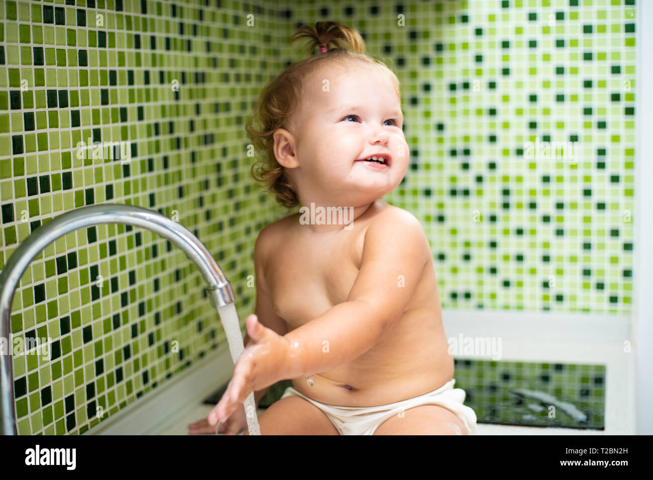 Baby in der Wanne. Baby sitzt in der Küche Spüle und berührte das Wasser aus dem Hahn. baby wäscht seine Hände. Stockfoto