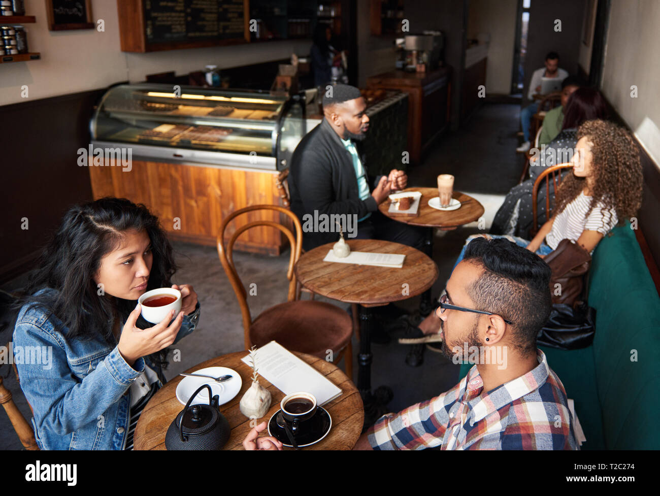 Verschiedene Gruppe junger Menschen an Tischen sitzen in einem angesagten Cafes Kaffee trinken und reden Stockfoto
