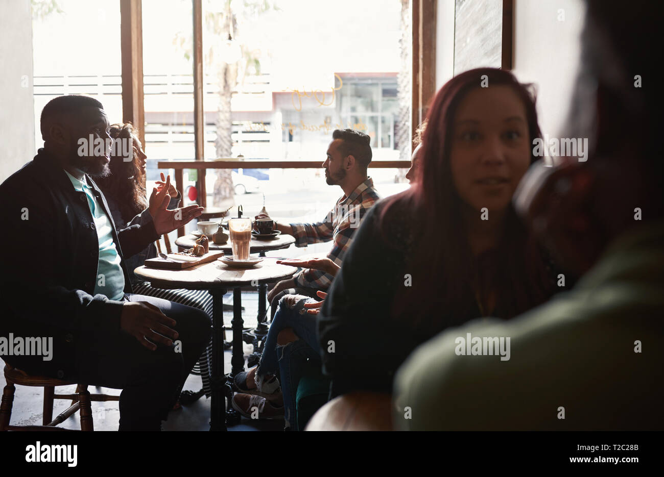 Vielfältige Gruppe von jungen Freunden Cafe Kaffee trinken und reden, während an den Tischen sitzen zusammen in einem trendigen Stockfoto
