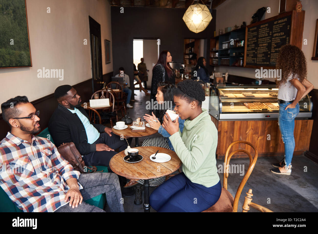 Vielfältige Gruppe von lächelnden jungen Menschen an Tischen sitzen in einem angesagten Cafes Kaffee trinken und reden Stockfoto