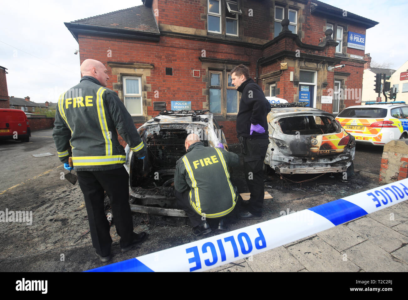 Feuerwehrleute kümmern sich um die zwei Polizeiautos, die nach dem Feuer außerhalb des Goldthorpe Polizei in South Yorkshire in einem mutmaßlichen Brandanschlag gesetzt wird zerstört wurden. Stockfoto