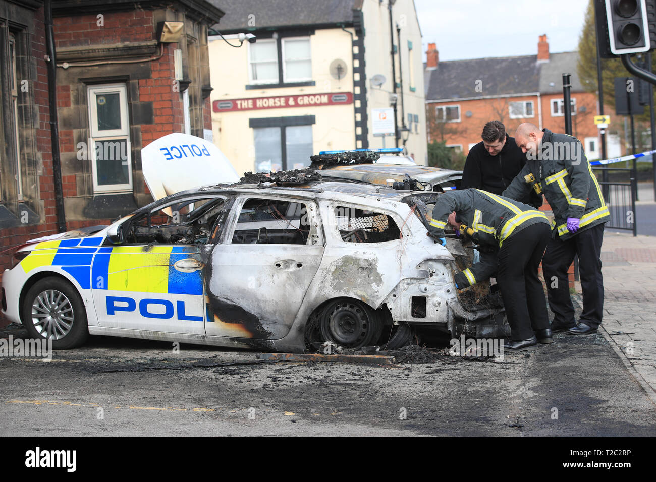 Feuerwehrleute kümmern sich um die zwei Polizeiautos, die nach dem Feuer außerhalb des Goldthorpe Polizei in South Yorkshire in einem mutmaßlichen Brandanschlag gesetzt wird zerstört wurden. Stockfoto