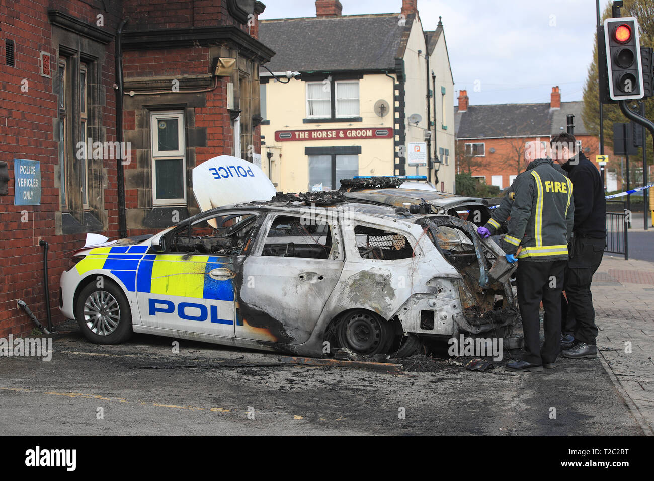 Feuerwehrleute kümmern sich um die zwei Polizeiautos, die nach dem Feuer außerhalb des Goldthorpe Polizei in South Yorkshire in einem mutmaßlichen Brandanschlag gesetzt wird zerstört wurden. Stockfoto