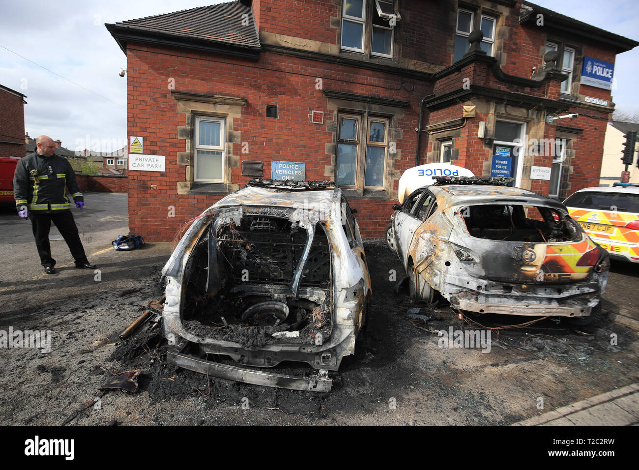 Feuerwehrleute kümmern sich um die zwei Polizeiautos, die nach dem Feuer außerhalb des Goldthorpe Polizei in South Yorkshire in einem mutmaßlichen Brandanschlag gesetzt wird zerstört wurden. Stockfoto