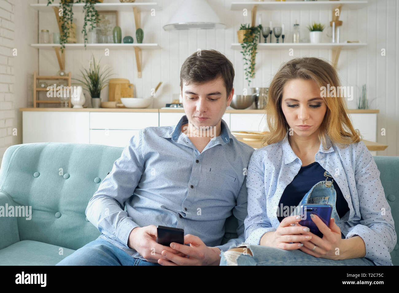 Schöne Mädchen Kerl in Denim Kleidung sitzen auf der gemütlichen blauen Sofa im Internet surfen in Smartphones in der modernen Küche Stockfoto