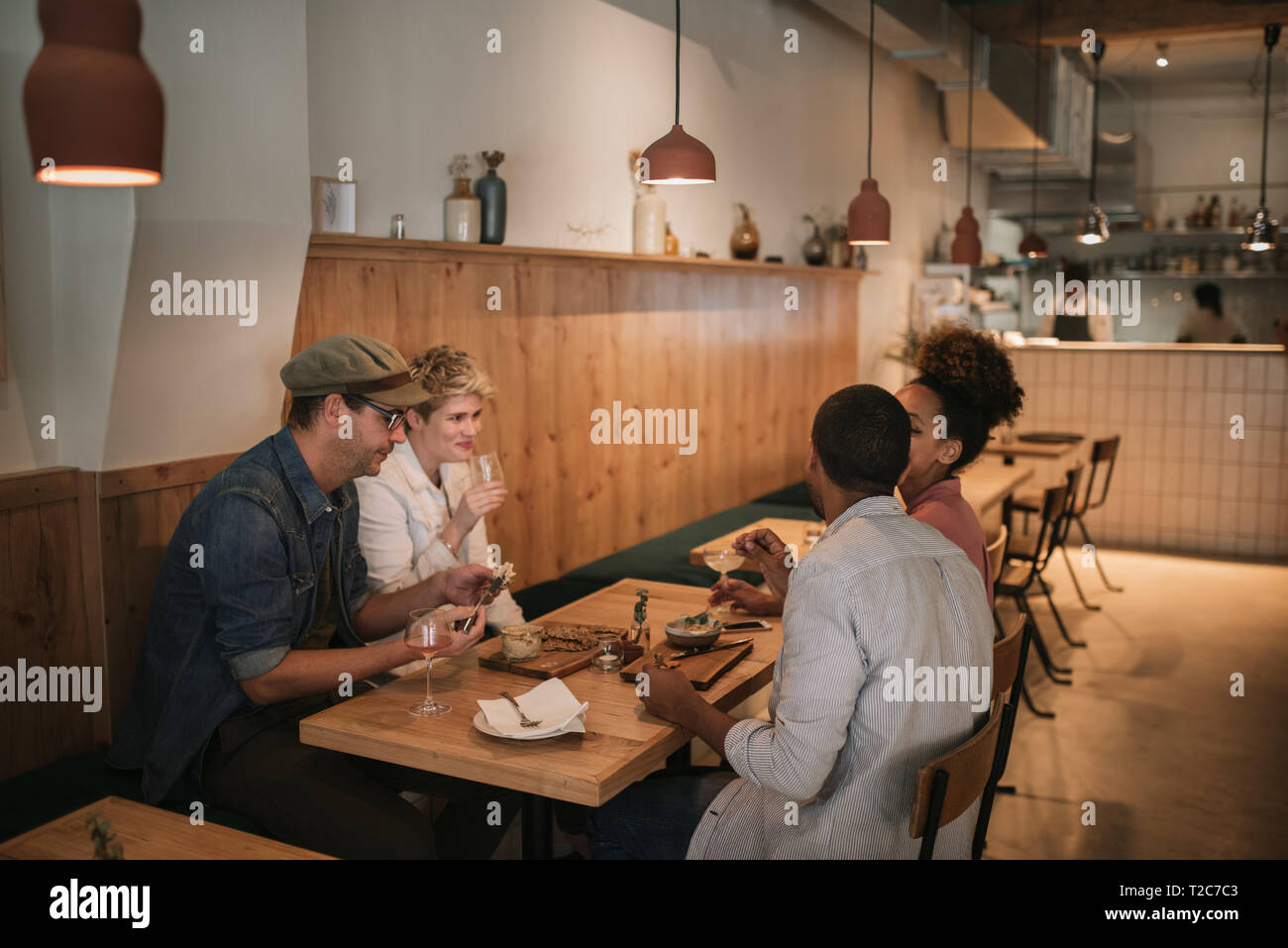 Vielfältige Gruppe von lächelnden jungen Freunde gemeinsame Essen beim zusammen an einem Tisch sitzen in einer angesagten Bar Stockfoto